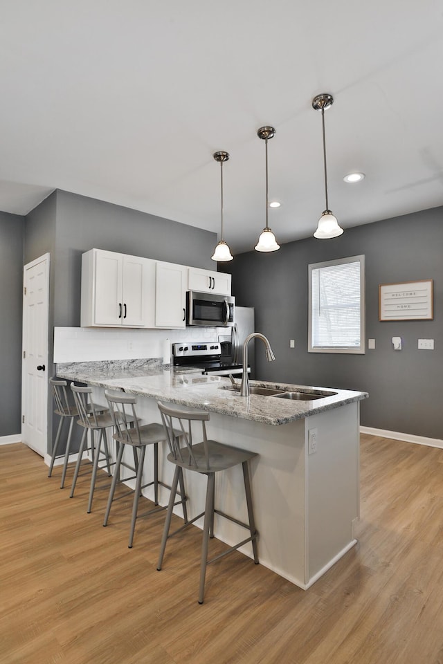 kitchen featuring appliances with stainless steel finishes, a kitchen breakfast bar, a peninsula, white cabinetry, and a sink