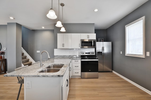 kitchen featuring stainless steel appliances, light wood-style floors, white cabinets, a sink, and baseboards