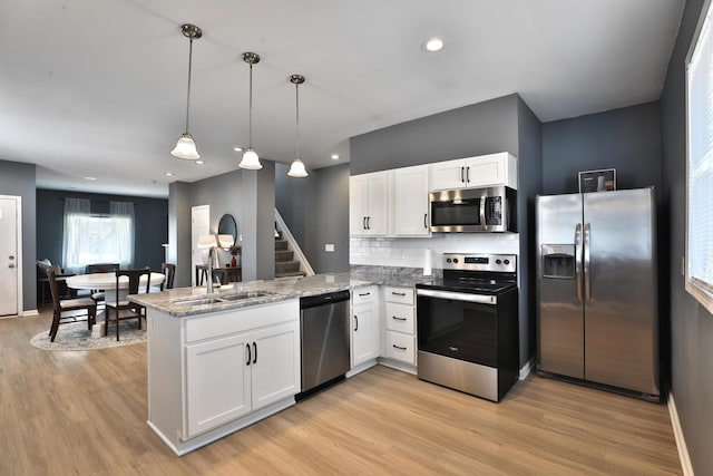 kitchen with a peninsula, white cabinets, stainless steel appliances, and a sink