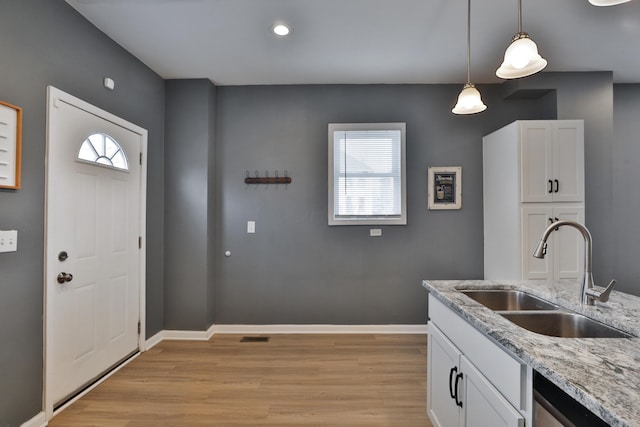 kitchen featuring light wood-style flooring, a sink, baseboards, white cabinets, and dishwasher