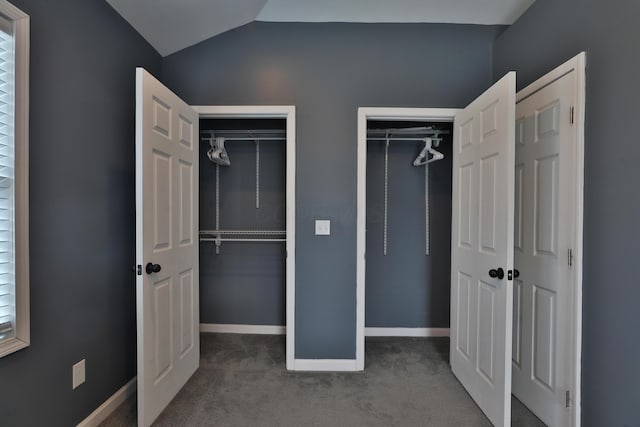 unfurnished bedroom featuring two closets, baseboards, vaulted ceiling, and carpet flooring