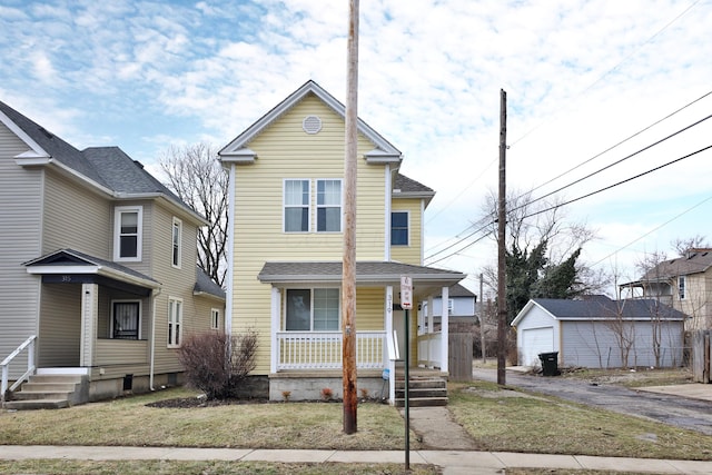 traditional-style house featuring an outbuilding, a detached garage, covered porch, driveway, and a front lawn