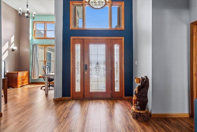 entrance foyer featuring a towering ceiling, an inviting chandelier, baseboards, and wood finished floors