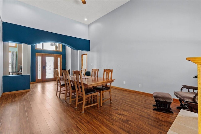 dining area with high vaulted ceiling, baseboards, arched walkways, and wood finished floors