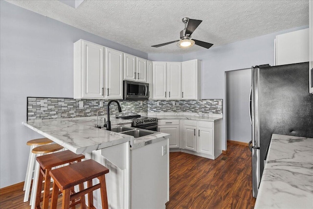 kitchen featuring a breakfast bar area, stainless steel appliances, white cabinets, light stone countertops, and a peninsula