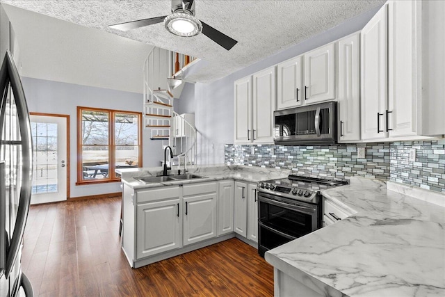 kitchen with appliances with stainless steel finishes, a peninsula, light stone countertops, white cabinetry, and a sink