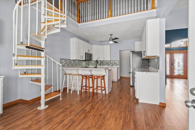 kitchen featuring white cabinets, stainless steel microwave, a breakfast bar area, dark wood-style flooring, and light countertops