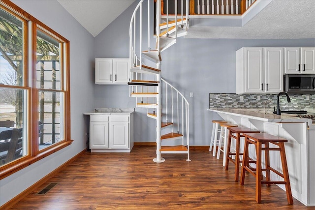 kitchen featuring a kitchen breakfast bar, dark wood-style flooring, stainless steel microwave, and white cabinets