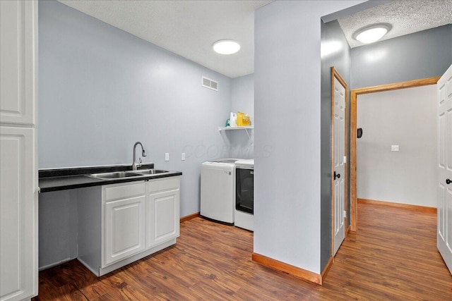 kitchen featuring visible vents, white cabinets, dark countertops, washing machine and dryer, and a sink