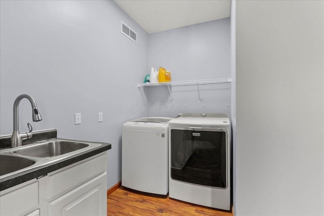 laundry room featuring cabinet space, visible vents, light wood-style floors, a sink, and independent washer and dryer