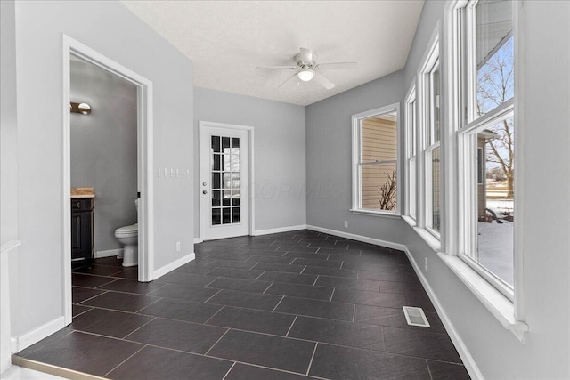 unfurnished room featuring a ceiling fan, dark tile patterned floors, visible vents, and baseboards