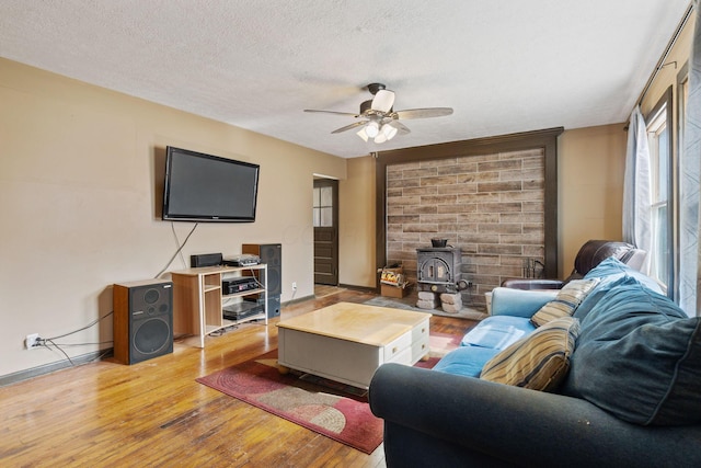 living room with baseboards, a ceiling fan, a wood stove, a textured ceiling, and light wood-style floors