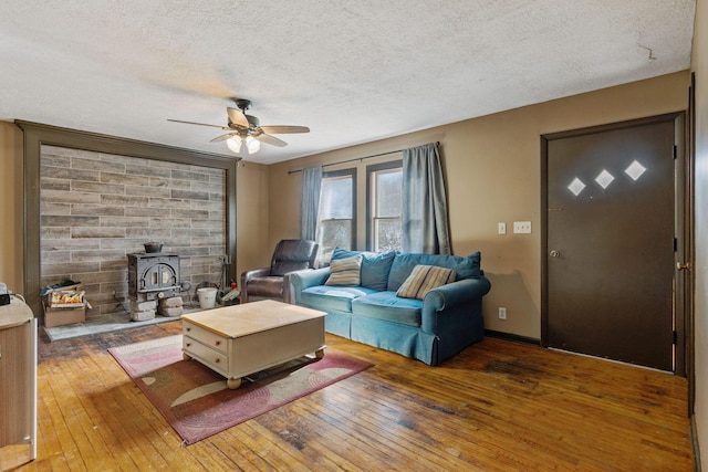 living room featuring dark wood-type flooring, a wood stove, ceiling fan, and a textured ceiling