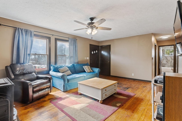 living area featuring hardwood / wood-style flooring, ceiling fan, baseboards, and a textured ceiling