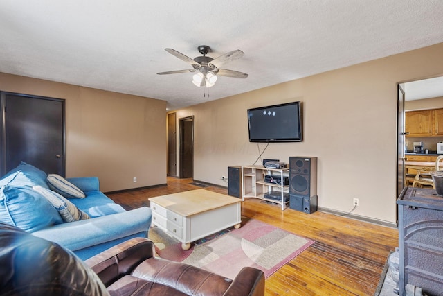 living area with a textured ceiling, wood finished floors, a ceiling fan, and baseboards