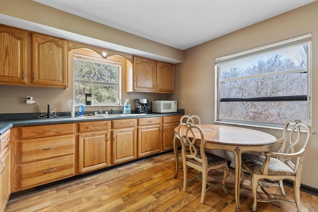 kitchen featuring dark countertops, white microwave, light wood-style floors, brown cabinetry, and a sink