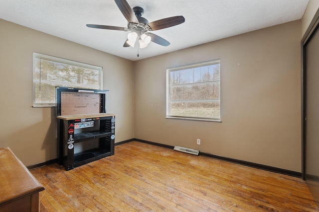 interior space with a textured ceiling, light wood-type flooring, visible vents, and baseboards