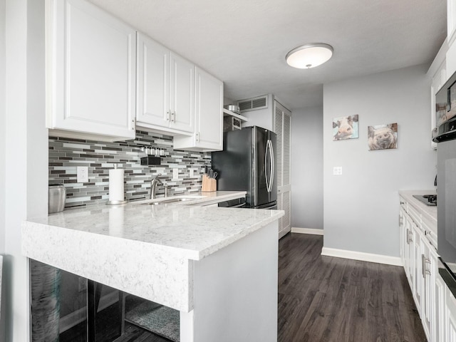 kitchen with dark wood-style flooring, backsplash, freestanding refrigerator, white cabinetry, and a sink