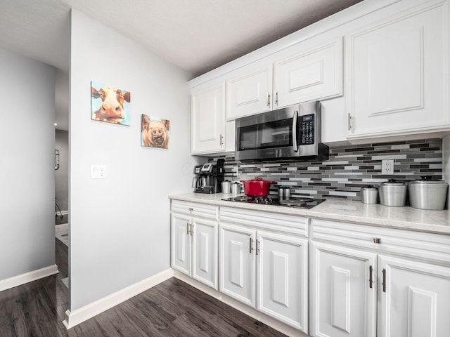 kitchen with decorative backsplash, stainless steel microwave, light countertops, black cooktop, and white cabinetry