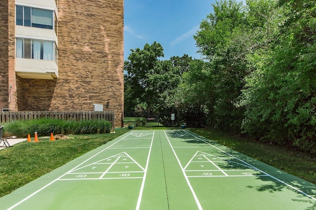 view of community featuring shuffleboard, a lawn, and fence