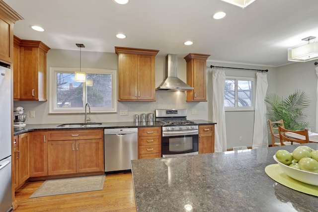 kitchen featuring brown cabinets, stainless steel appliances, light wood-type flooring, wall chimney range hood, and a sink