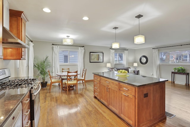 kitchen featuring light wood finished floors, brown cabinetry, wall chimney exhaust hood, white dishwasher, and stainless steel range with gas cooktop