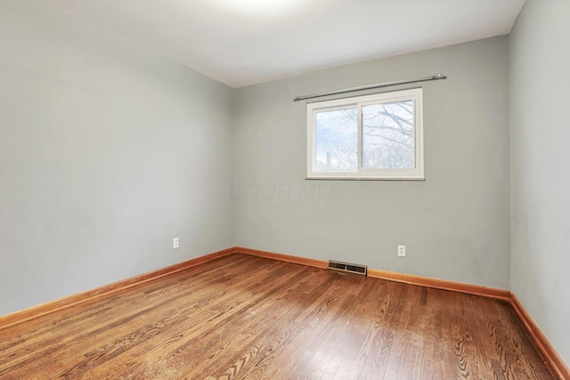 unfurnished room with wood finished floors, visible vents, and baseboards