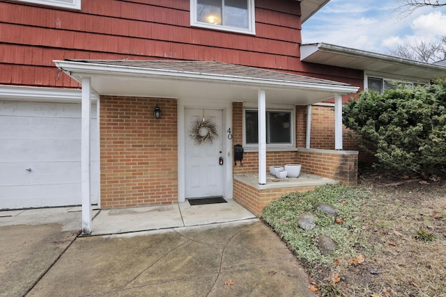 view of exterior entry featuring covered porch, roof with shingles, and brick siding