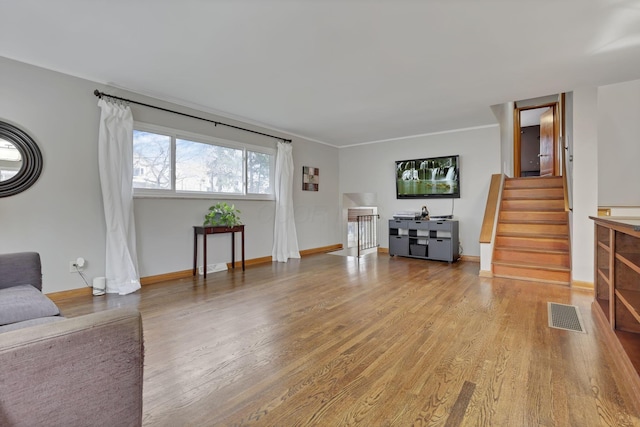 living room with stairs, visible vents, baseboards, and wood finished floors