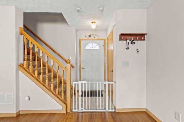 entrance foyer with baseboards, visible vents, wood finished floors, stairs, and a textured ceiling