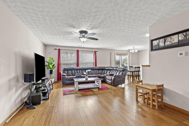 living room featuring ceiling fan with notable chandelier, a textured ceiling, light wood-style flooring, and baseboards