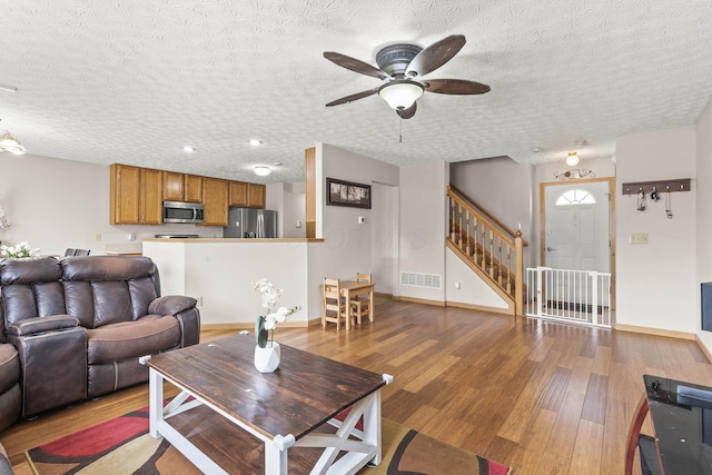 living area featuring wood finished floors, a ceiling fan, visible vents, stairs, and baseboards