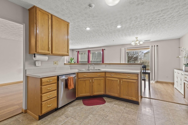 kitchen with a sink, a peninsula, light countertops, and stainless steel dishwasher