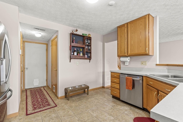 kitchen with light countertops, visible vents, appliances with stainless steel finishes, brown cabinetry, and a textured ceiling