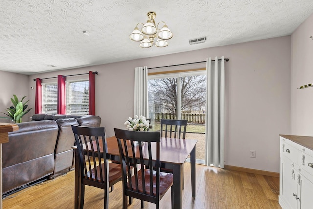 dining room featuring visible vents, baseboards, a textured ceiling, light wood-style floors, and a chandelier