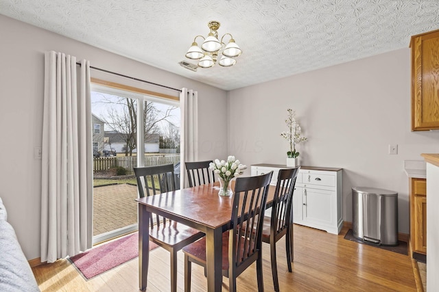 dining space featuring a textured ceiling, light wood finished floors, visible vents, and an inviting chandelier