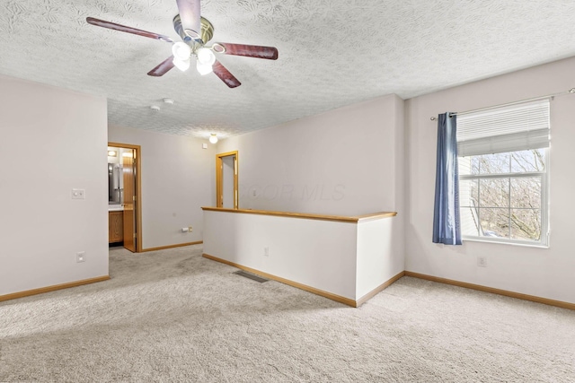 carpeted spare room featuring a textured ceiling, a ceiling fan, visible vents, and baseboards