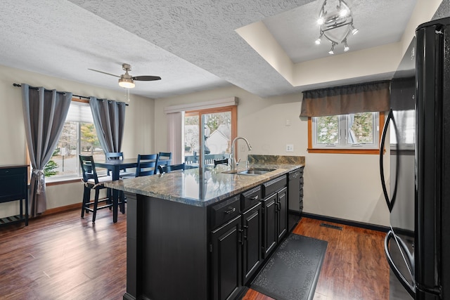 kitchen with stone countertops, dark cabinets, a sink, dark wood-style floors, and black appliances