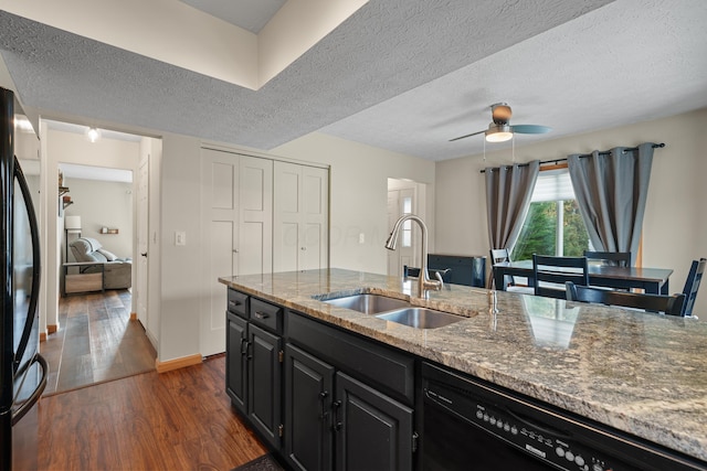 kitchen featuring dark cabinets, a sink, light stone counters, and black appliances