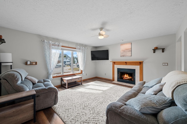 living room featuring a tile fireplace, ceiling fan, a textured ceiling, and wood finished floors