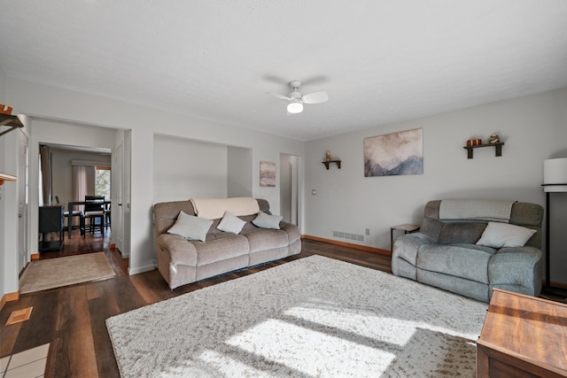 living room with dark wood-style flooring, a fireplace, visible vents, ceiling fan, and baseboards