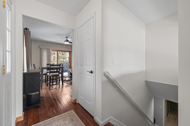 hall with dark wood-style flooring, baseboards, and an upstairs landing