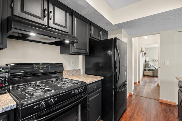 kitchen with dark wood-style floors, range hood, light countertops, dark cabinetry, and black appliances