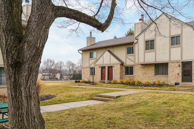 english style home with brick siding, a chimney, a front yard, and stucco siding