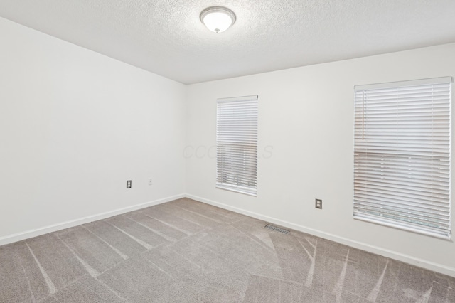 carpeted empty room featuring a textured ceiling, visible vents, and baseboards