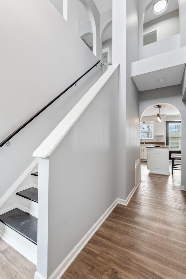 staircase featuring arched walkways, wood finished floors, a towering ceiling, and baseboards