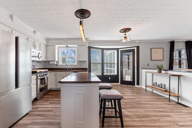 kitchen featuring dark countertops, hanging light fixtures, appliances with stainless steel finishes, white cabinetry, and a sink