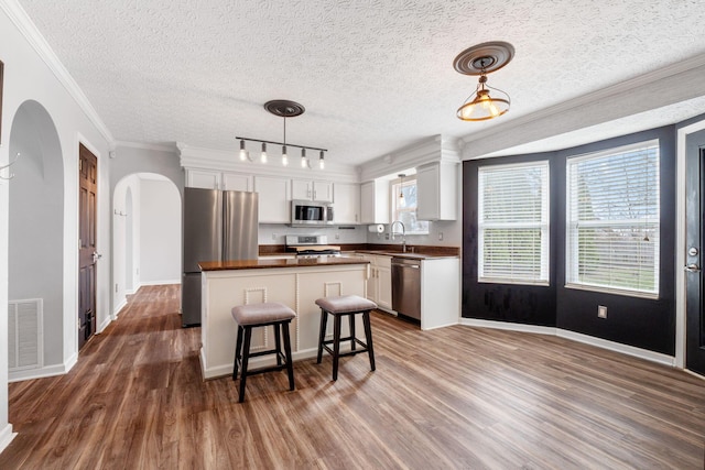 kitchen featuring visible vents, a center island, stainless steel appliances, white cabinetry, and pendant lighting