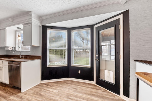 kitchen with white cabinets, dark countertops, stainless steel dishwasher, pendant lighting, and a sink