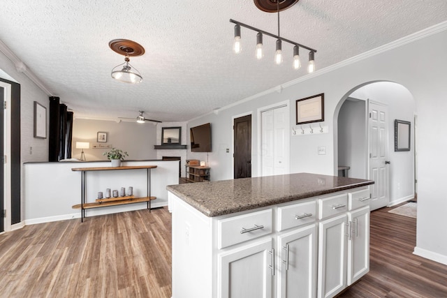 kitchen featuring white cabinetry, open floor plan, a center island, dark stone countertops, and decorative light fixtures